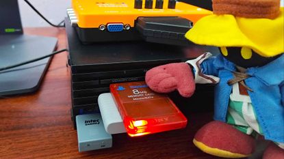Vivi plush from Final Fantasy 9 posed next to red PS2 memory card resting on controller receiver plugged into console.
