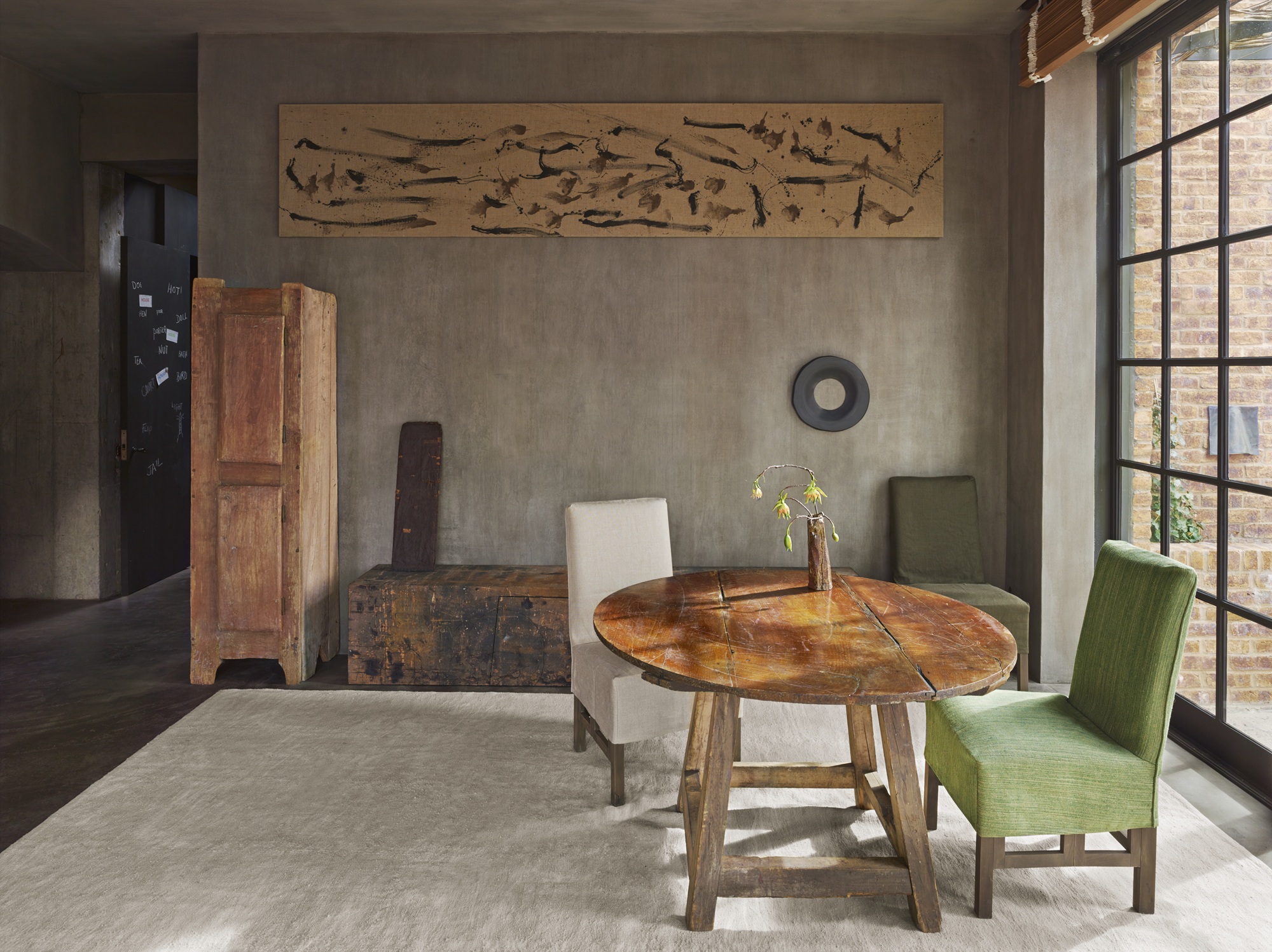 a rustic, minimalist hotel suite designed by axel vervoordt with a wooden table and green chair