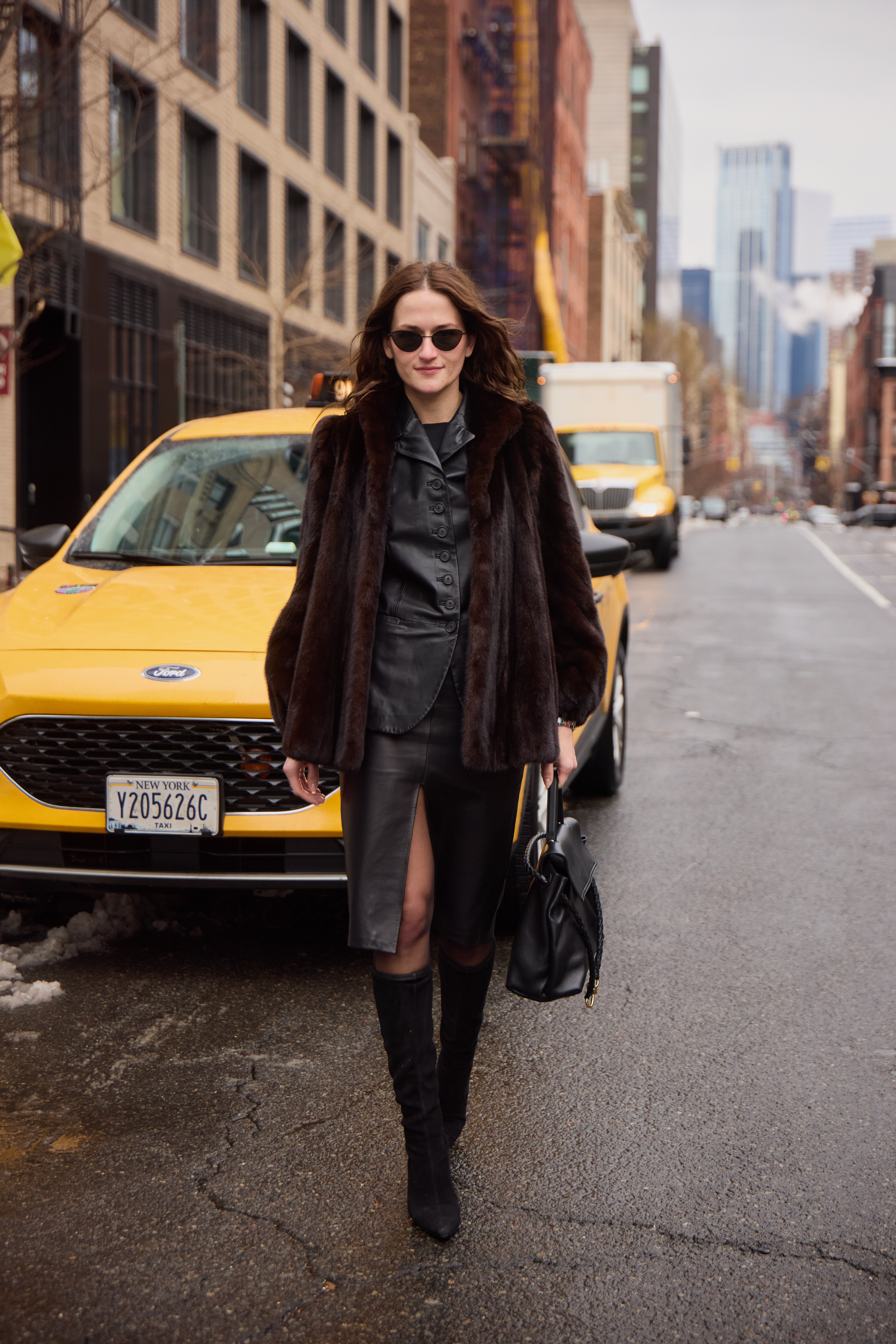 Eliza Huber wearing a brown fur coat, black leather jacket, black pencil skirt, black tights,  black suede boots, and black sunglasses while carrying a black Bottega Veneta Ciao Ciao bag outside of the Ulla Johnson show in Soho.