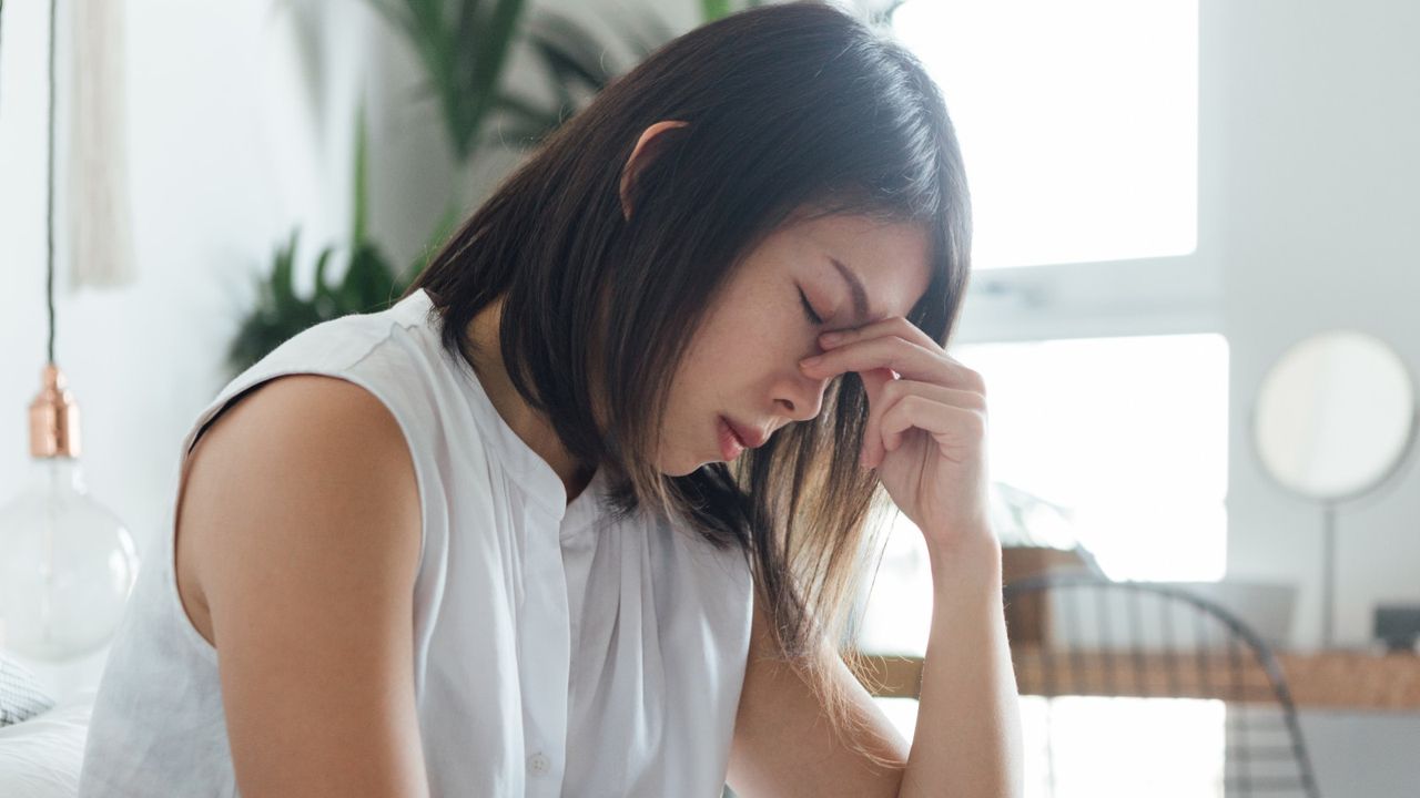 Young woman touching bridge of nose to relieve headache while resting in bed.