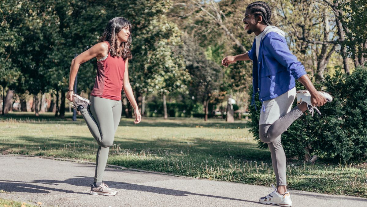 Female and male runners performing quad stretch in park