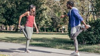 Female and male runners performing quad stretch in park