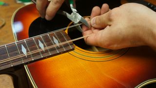Man cuts the strings off an acoustic guitar using wires cutters