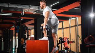 Man performs step-up exercise holding dumbbells in gym