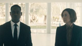 Sterling K. Brown wearing a dark suit and walking with Julianne Nicholson, also in a dark suit, in a white hallway.