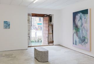 A gallery with white walls and abstract paintings on the wall. in the center of the room is a grey carved stone bench.