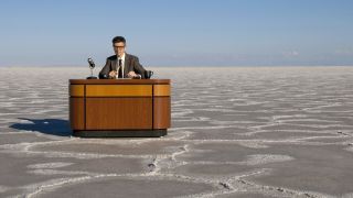 Ira Glass sitting in front of a desk on a salt flat in This American Life