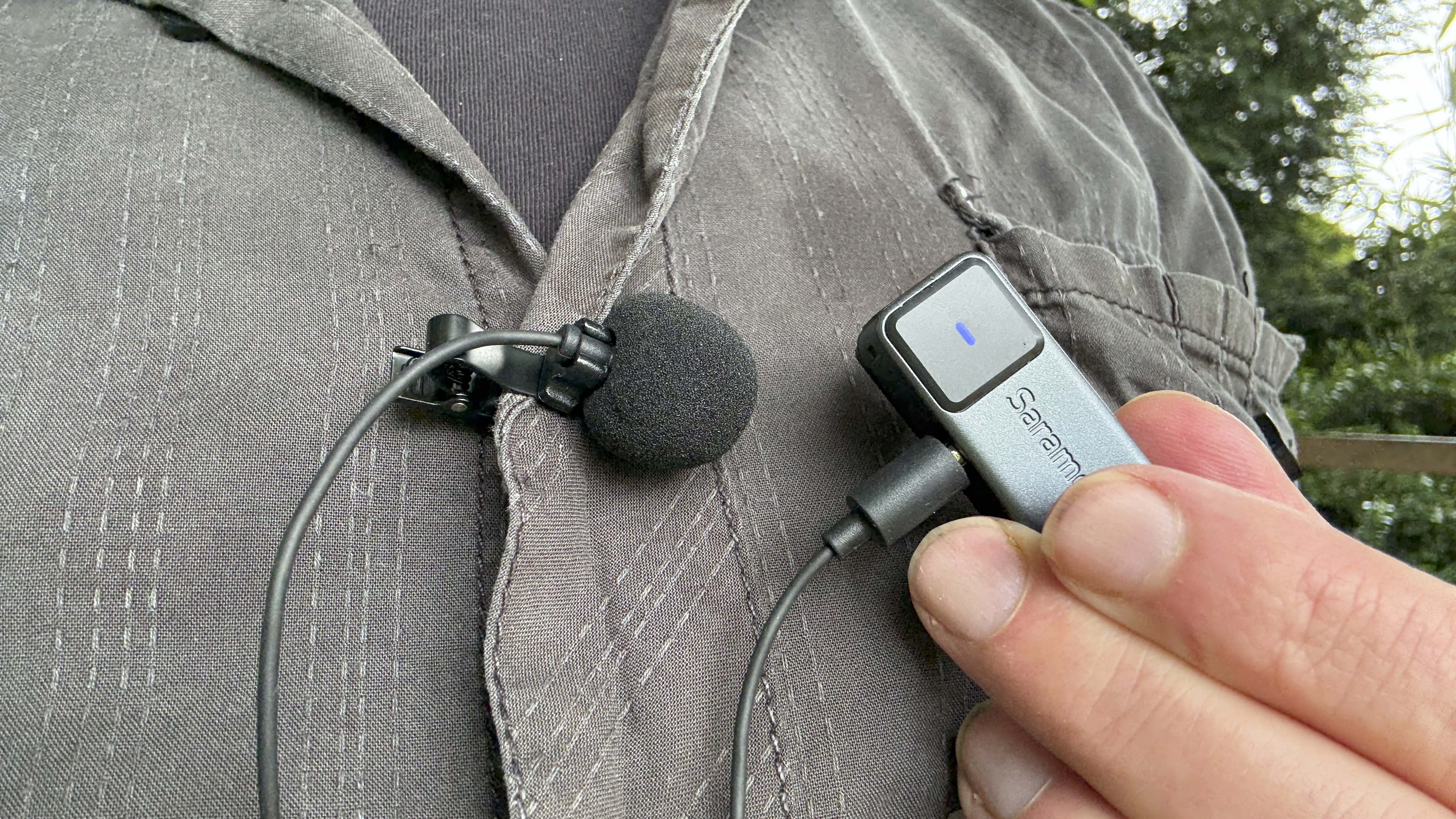 Close-up of a lavalier clip mic attached to a shirt. The mic is plugged into the transmitter mic
