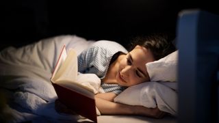 Woman awake in the middle of the night reading in bed after learning how to overcome sleep deprivation