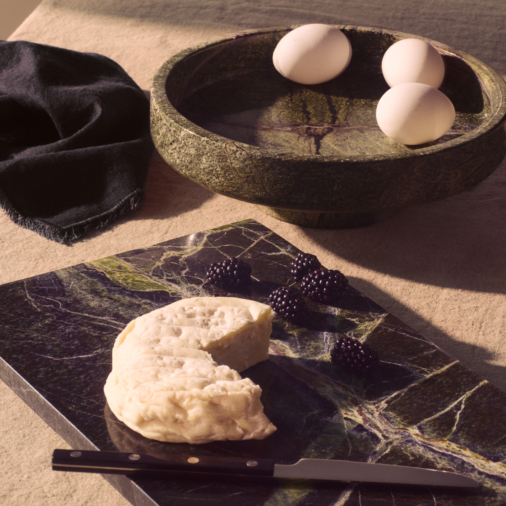 A dining table with a green marble serving home and black marble chopping board from the H&M Home autumn 2025 collection