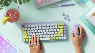 Logitech Pop Keys Emoji keyboard on a desk with a user resting their hand on the keys