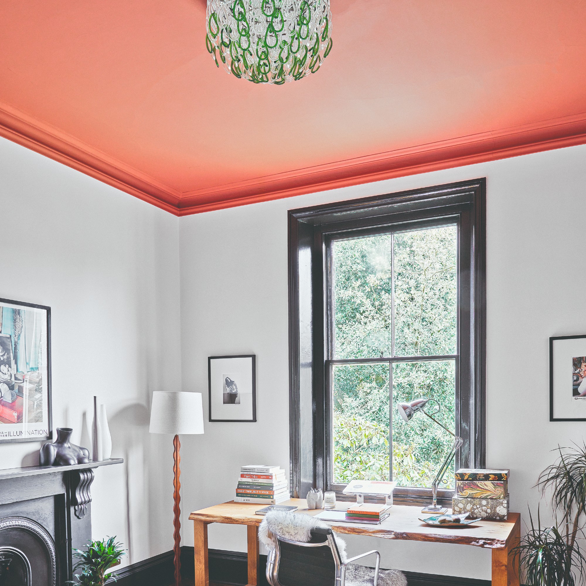 A home office with white walls and black-painted woodwork contrasted by a bold coral-painted ceiling with a shiny finish