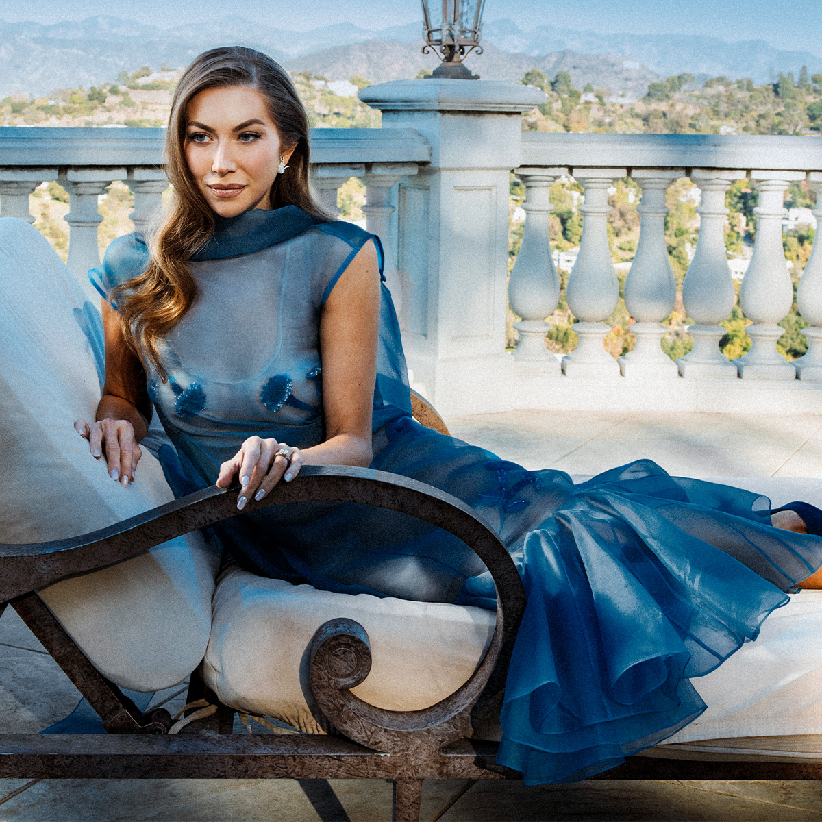 stassi schroeder wears a blue gown lying on a chair on a balcony overlooking los angeles