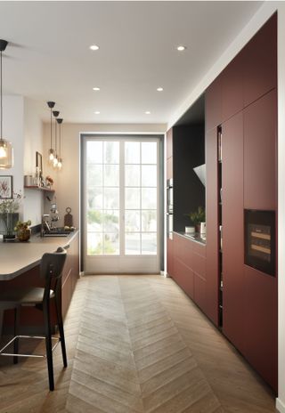 A red galley kitchen with slim french doors, herringbone flooring, sleek handleless cabinets and breakfast bar