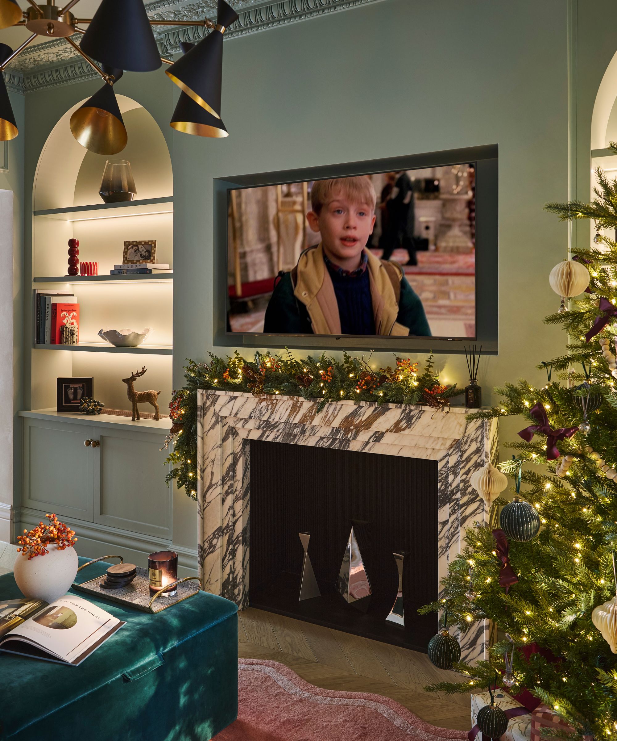 blue living room with arched alcove shelving decorated for christmas with a marble fireplace styled with a garland, a large tree in the corner, and the Home Alone movie on the TV screen