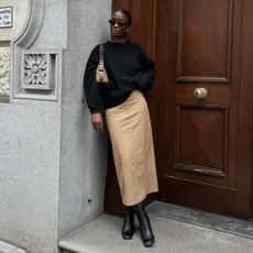 Woman wears black jumper, beige skirt and black boots