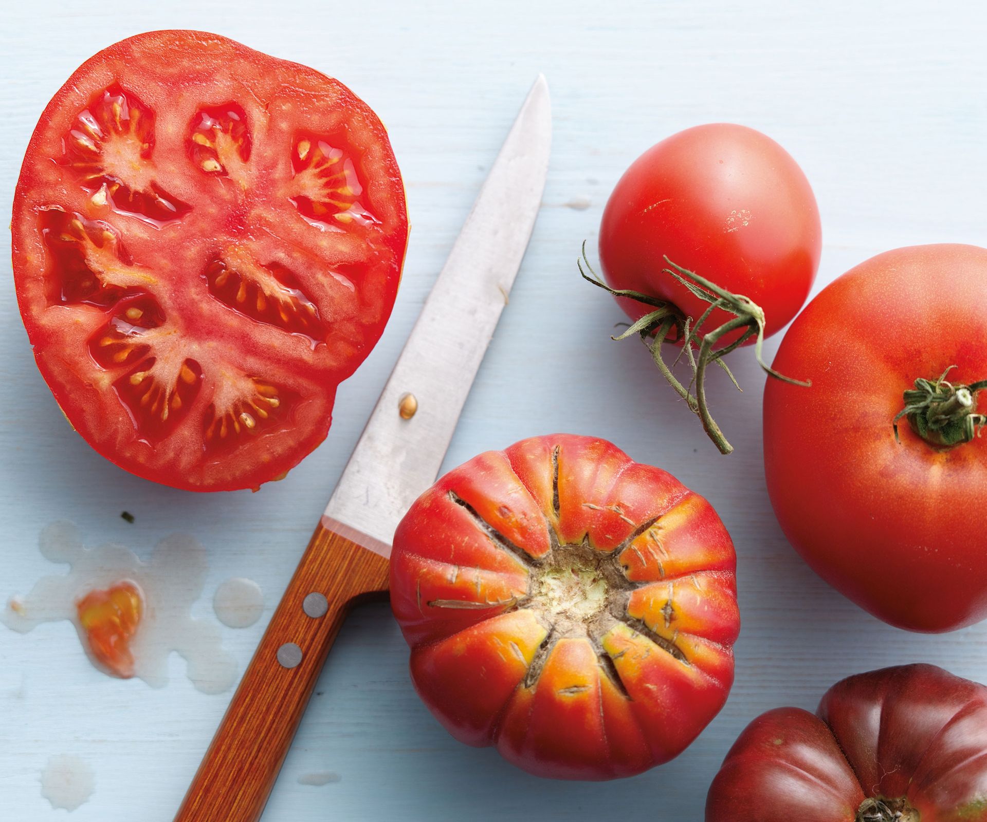 tomatoes and sliced tomatoes with wooden handled knife on kitchen work surface