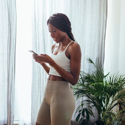 prime day pilates deals - woman in pilates clothes looking at her phone - getty images 1333812705