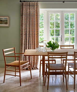 dining room image with wooden table and chairs and patterned curtain and light green walls