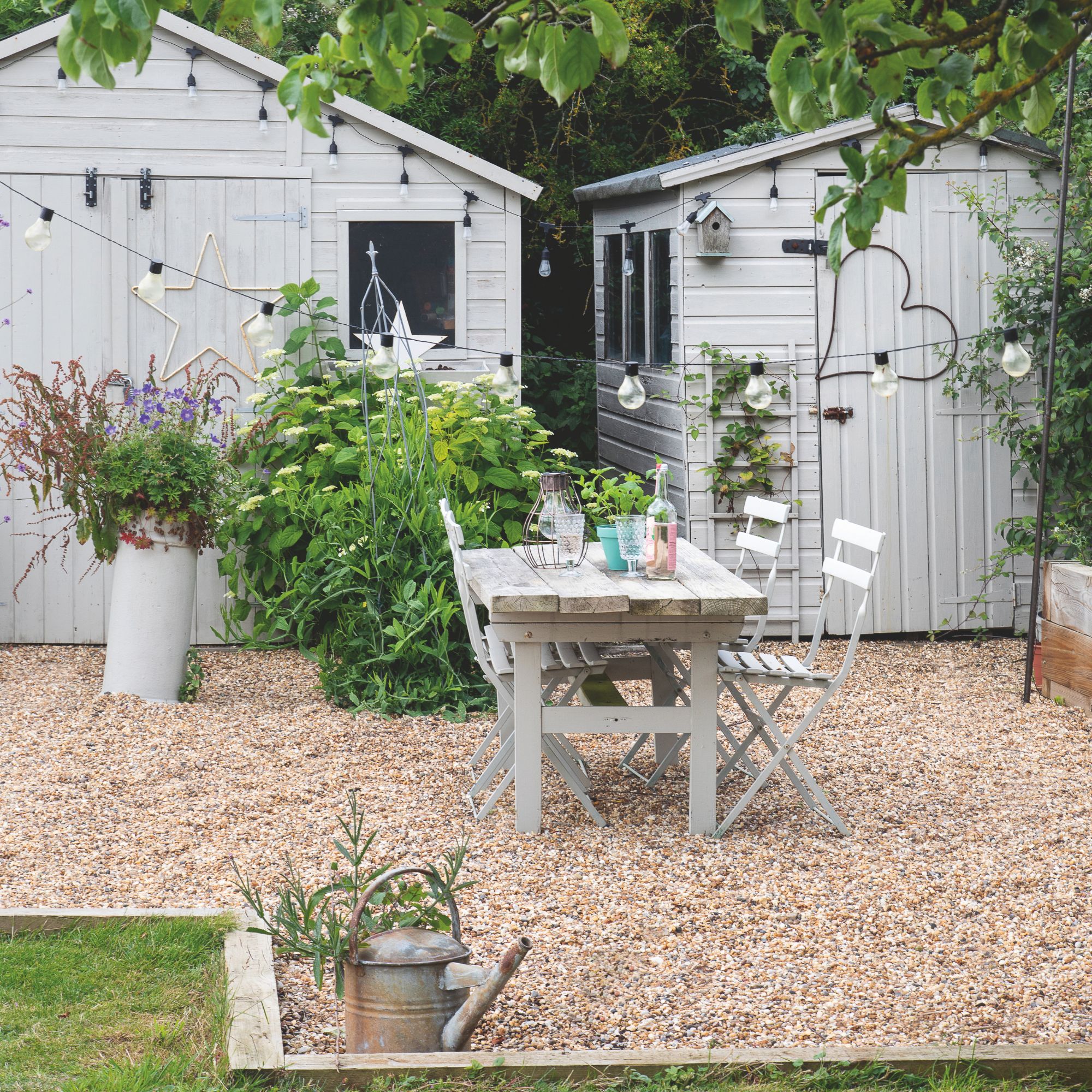 Graven garden area with wooden table and chairs on it and two sheds behind it