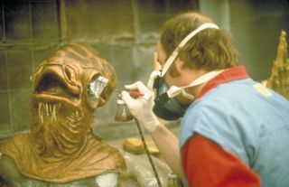 a man airbrushing a mask of an alien