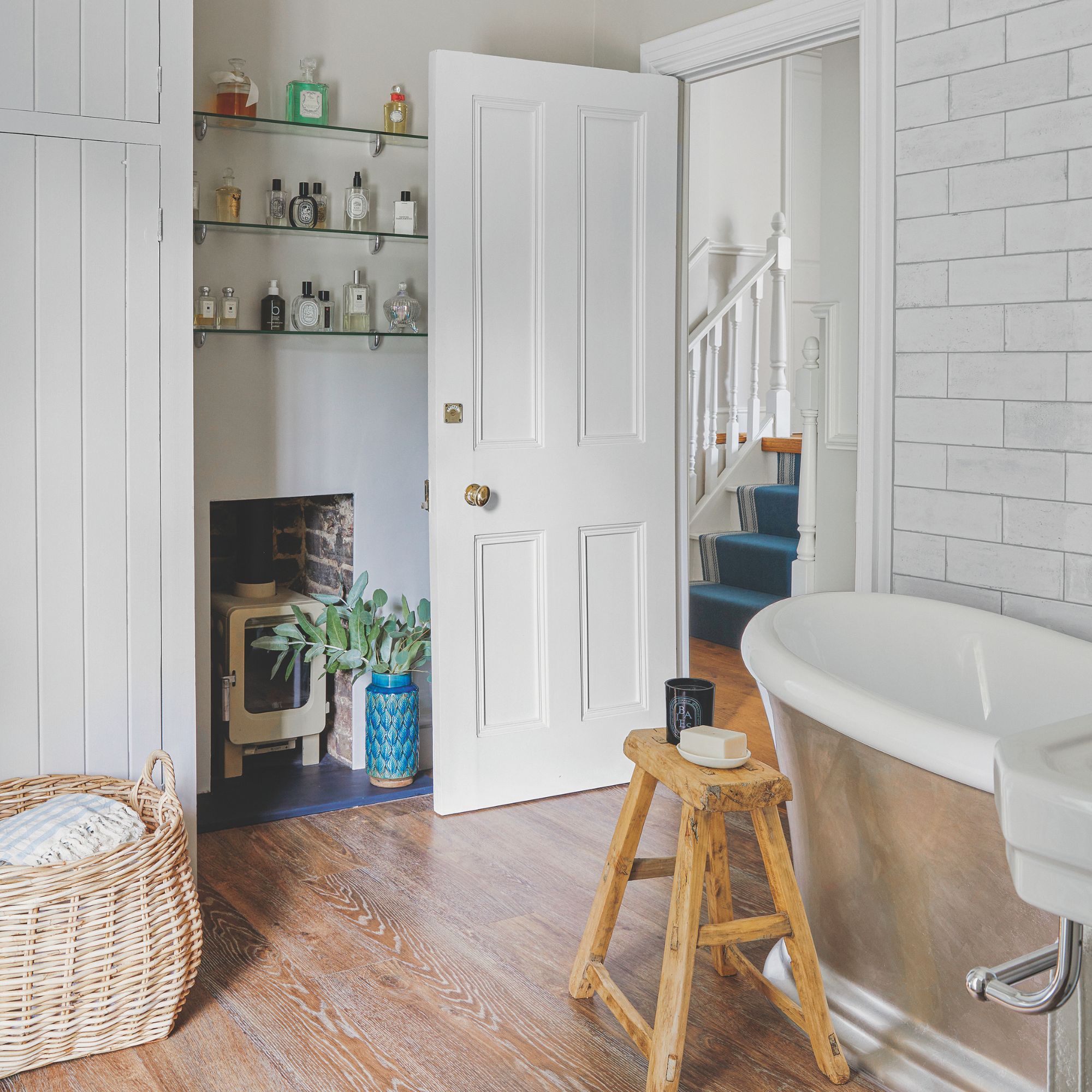 White tiled bathroom with a freestanding bath and a log burner in the corner