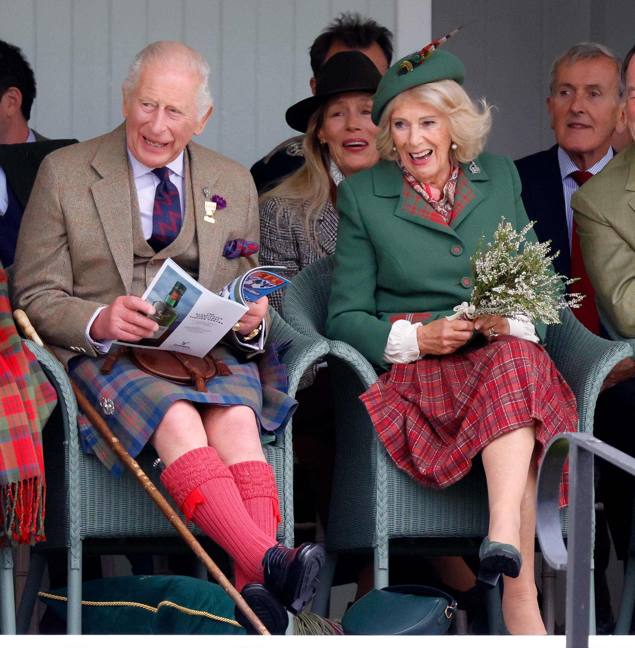King Charles in a kilt sitting next to Queen Camilla and laughing