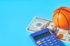 Basketball, calculator, and one hundred dollar bill on a bright blue background