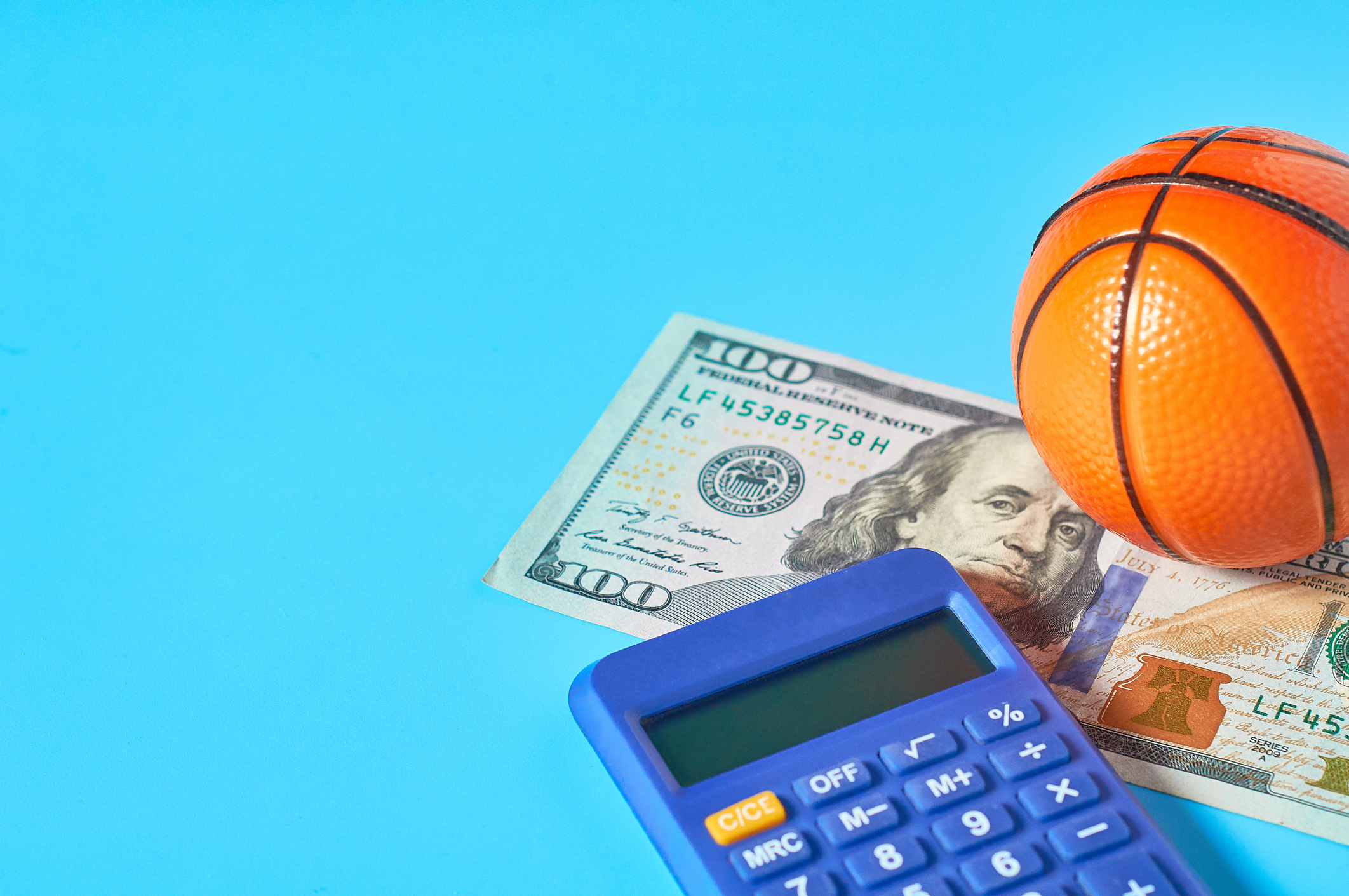Basketball, calculator, and one hundred dollar bill on a bright blue background