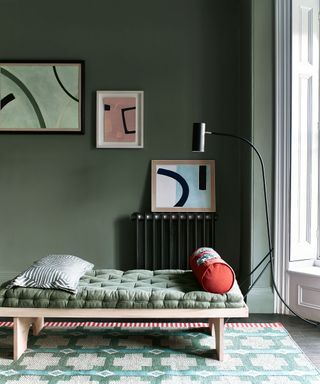 Modern, dark green living room with olive green paint, wooden bench and gallery wall of abstract art.