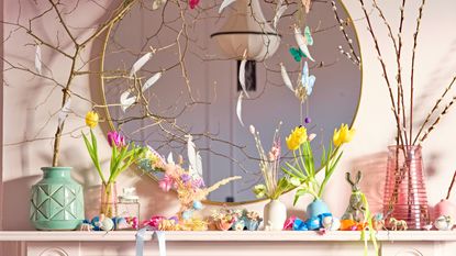 Easter mantelscape with pastel vases filled with fresh spring blooms, large round mirror on wall, wrapped confectionary, and playful animal figurines.
