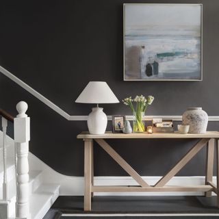 A dark grey hallway with a slim wooden console table and artwork on the wall