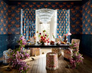 A dining room wall idea with blue and coral wallpapered walls, matching curtains and upholstered floral chairs