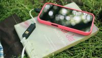An iFi Go Link 2 Max DAC plugged into an iPhone in a pink case lying on top of The Bell Jar by Silvia Plath.