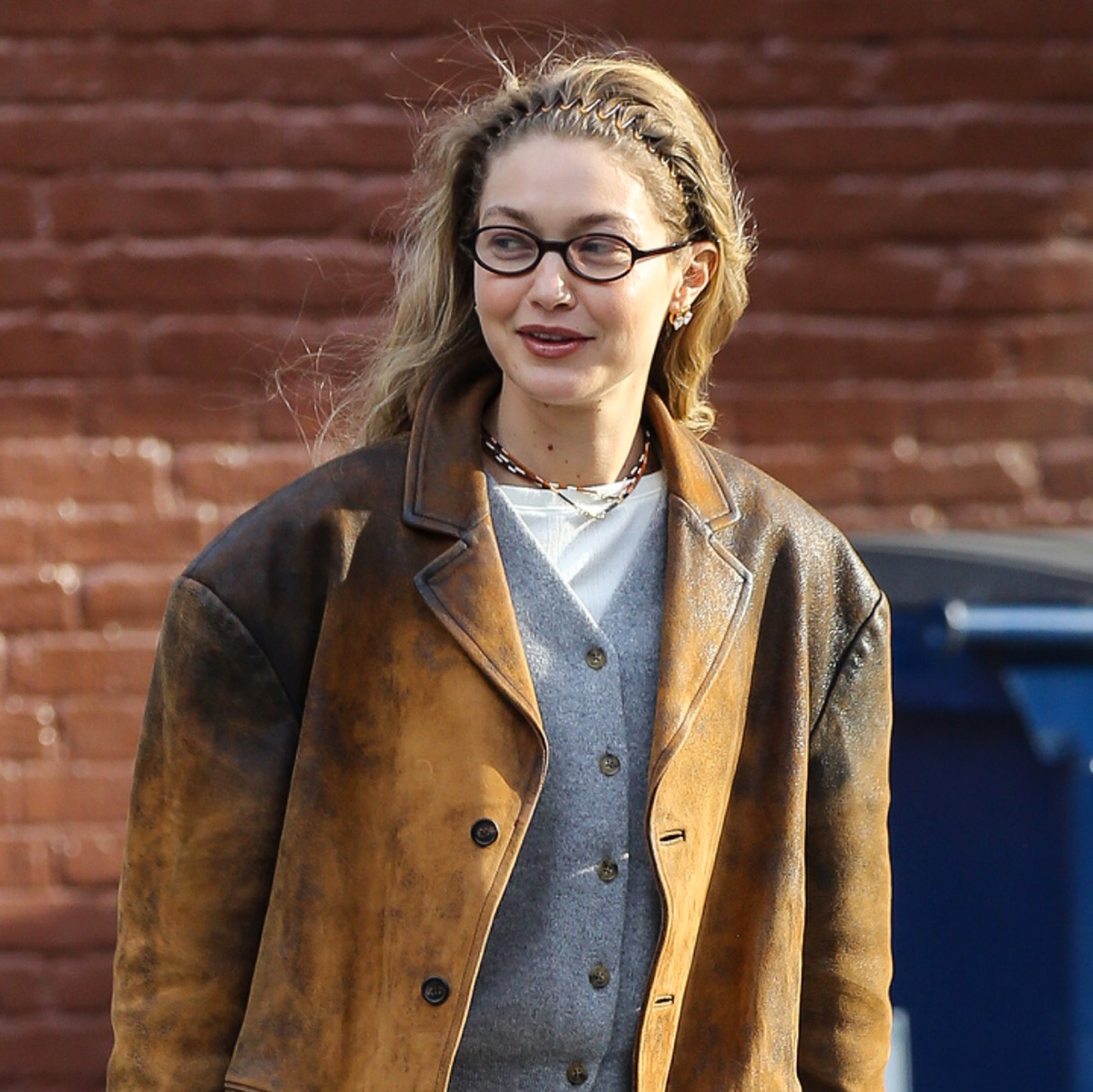 Gigi Hadid wearing a brown leather jacket with a gray cardigan and sweatpants and soft Miu Miu loafers