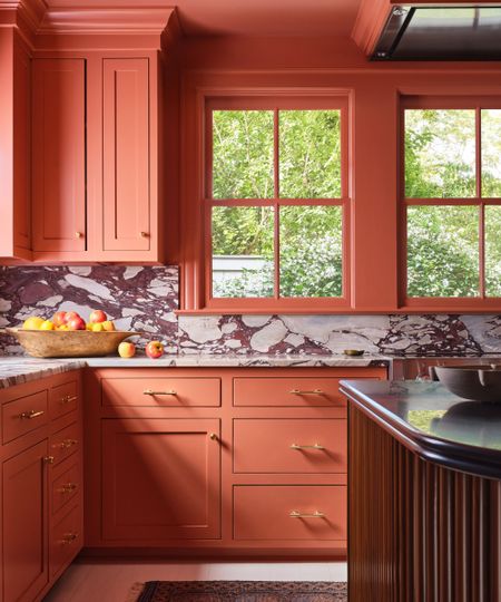 A terracotta kitchen with a wooden fluted island and marble countersplash