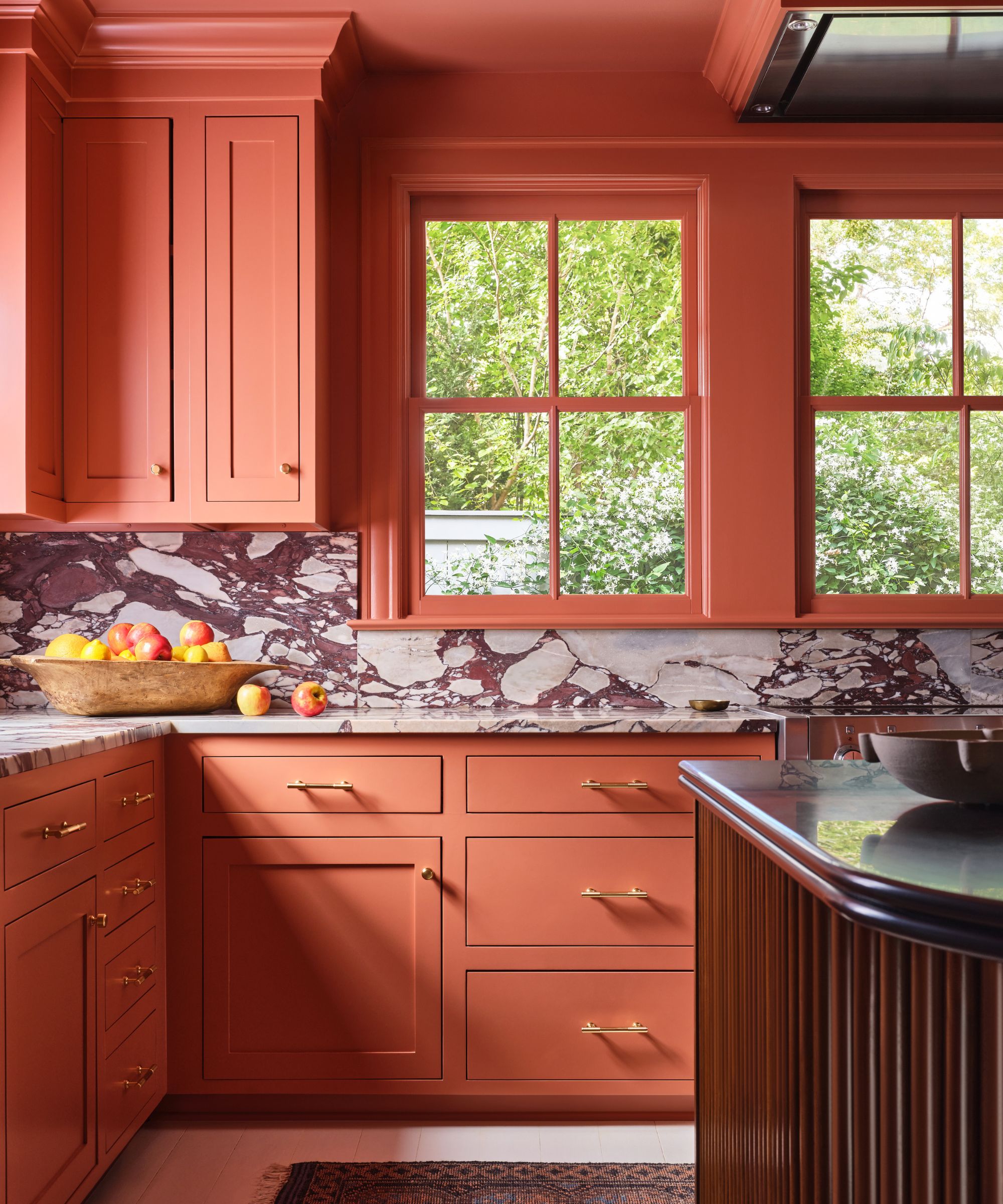 A terracotta kitchen with a wooden fluted island and marble countersplash