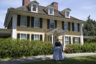 black woman in dress and hat, looking a colonial-era building