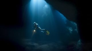 A diver in an underwater cave swimming in a ray of light