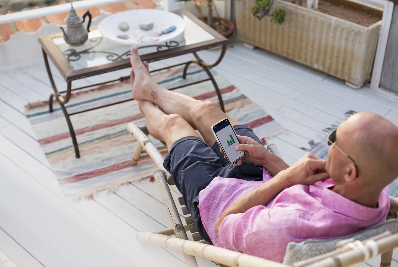 Man checking financial trading data on mobile phone while relaxing on deck chair