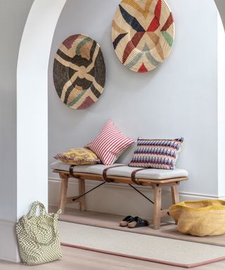 hallway with coloured rattan decorative art on white walls and wooden bench below