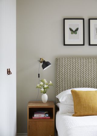 grey and white bedroom with upholstered headboard, yellow cushion, artwork, wall light, side table