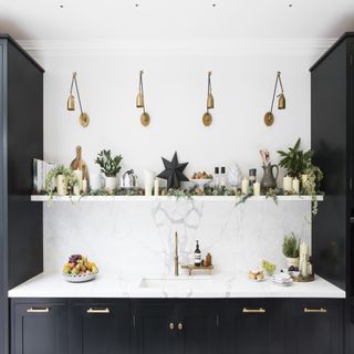 kitchen with white marble worktop and black cabinets, a shelf with house plants and gold wall lights