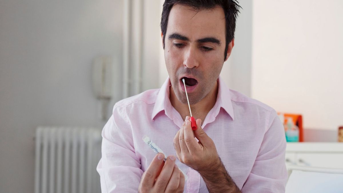 man in a button down shirt prepares to swab his cheek with a long cotton swab at home