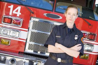 female firefighter stands in front of fire truck.