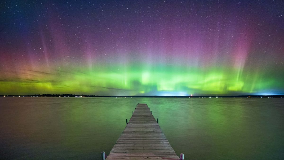 northern lights above Higgins Lake, Michigan appear as vibrant ribbons of green and purple light above the water. 