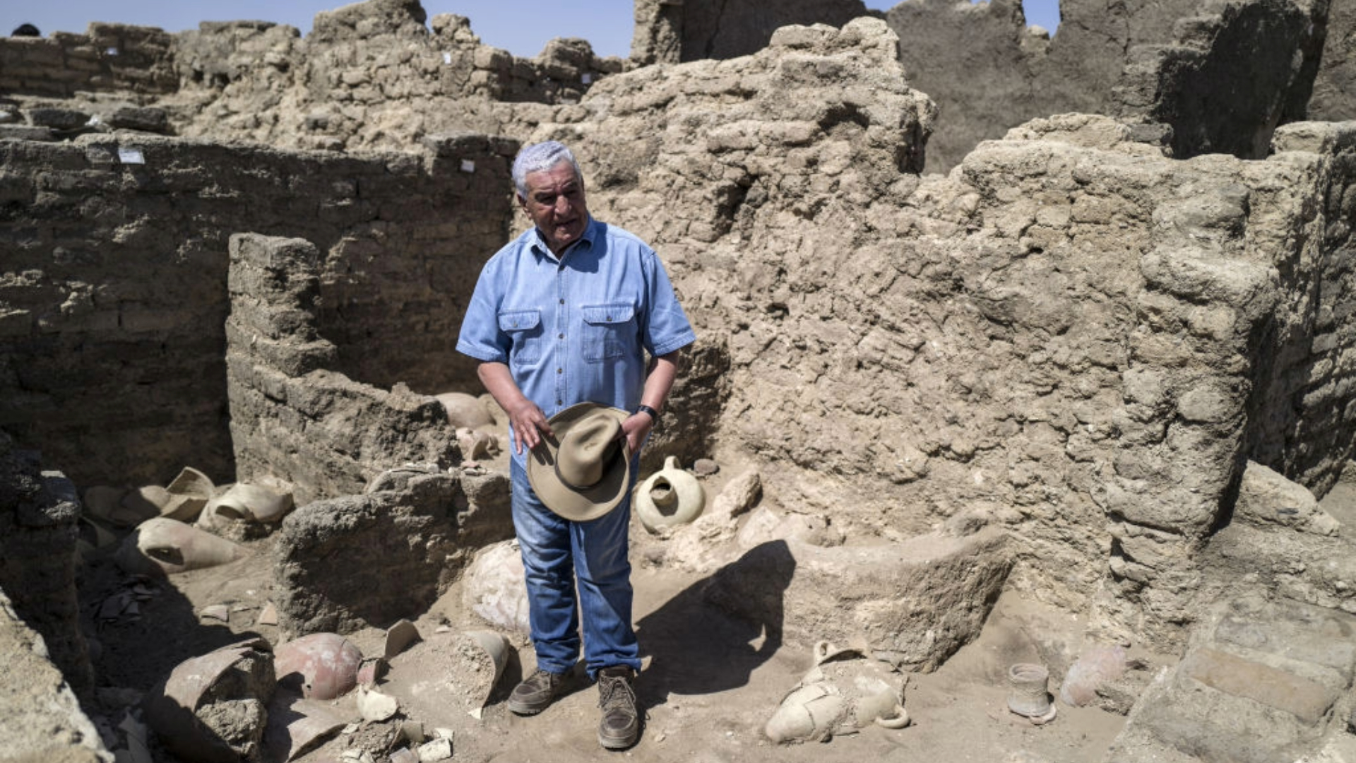 A man in a blue shirt stands next to brick ruins of an ancient city