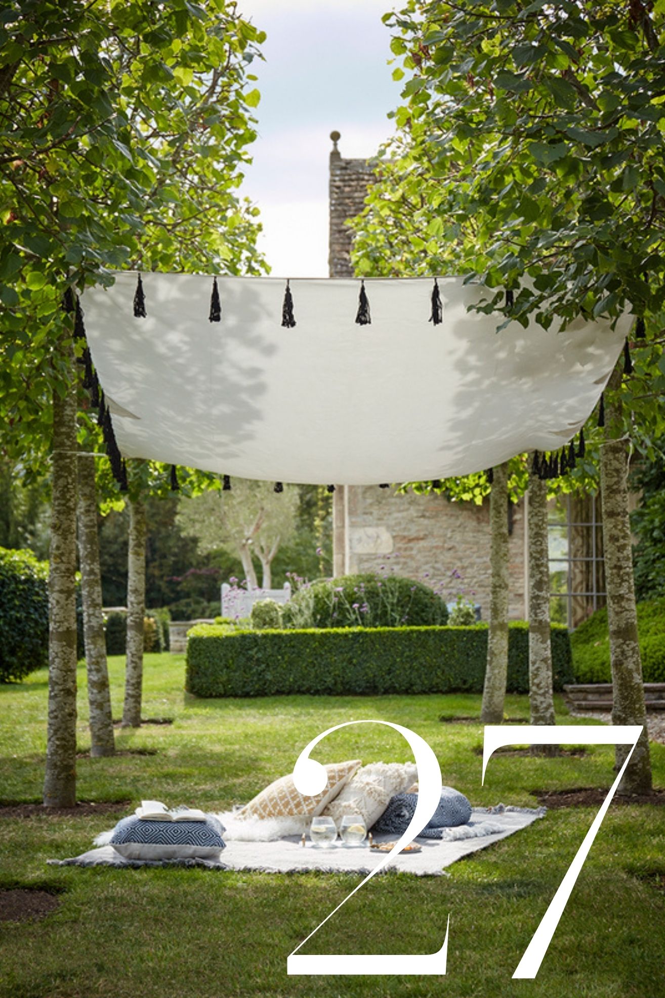 tasselled canopy strung up between trees in manicured garden with picnic blanket underneath