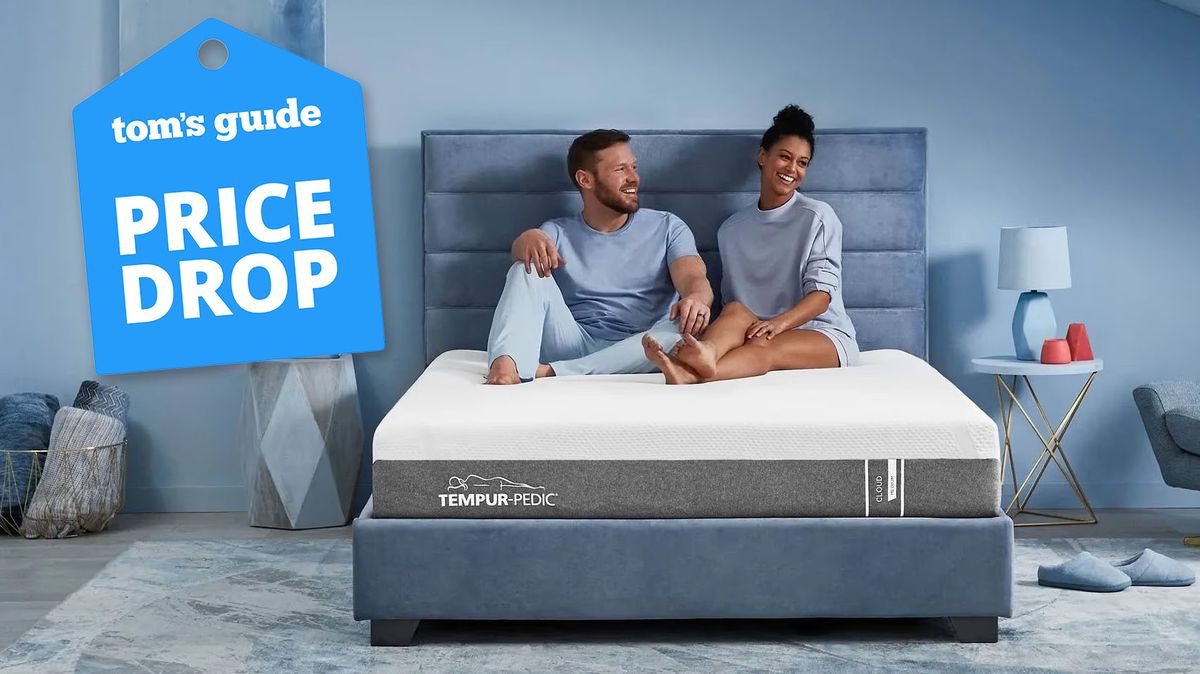 The Tempur-Pedic Tempur-Cloud mattress on a bed frame in a bedroom, a happy couple sits on top of the bed, a Tom&#039;s Guide price drop deal&#039;s graphic (left)