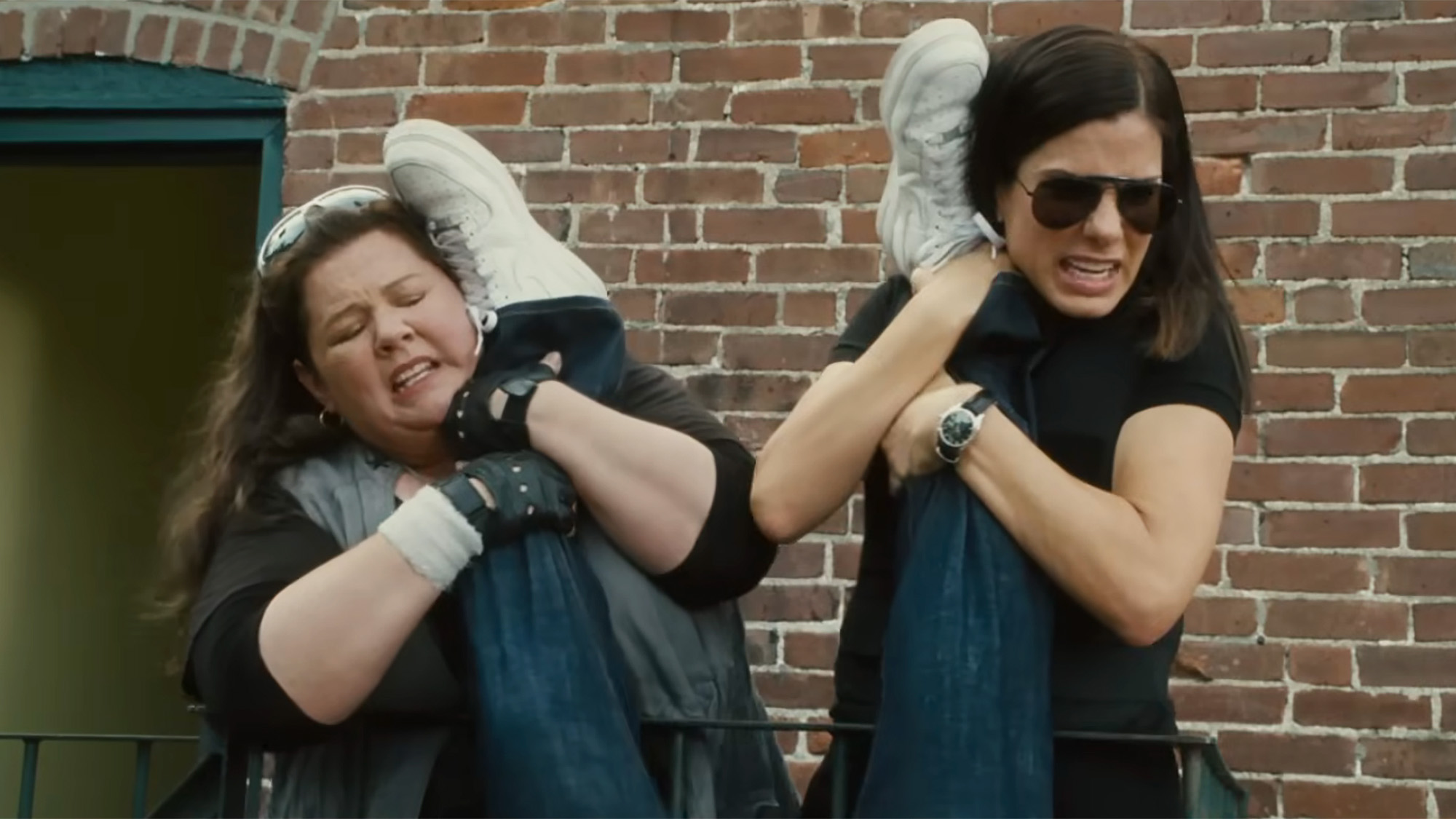 Sandra Bullock and Melissa McCarthy hold up a suspects legs while apprehending a bad guy in The Heat.